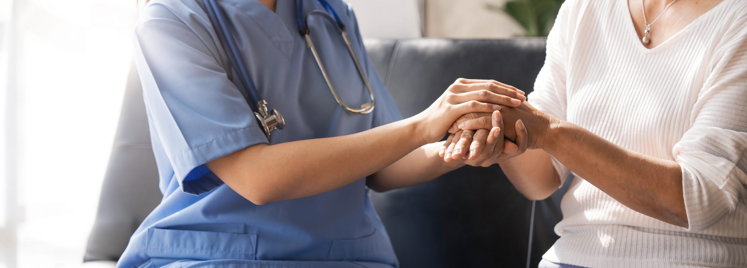 Closeup Happy patient is holding caregiver for a hand while spending time together. Elderly woman in nursing home and nurse.